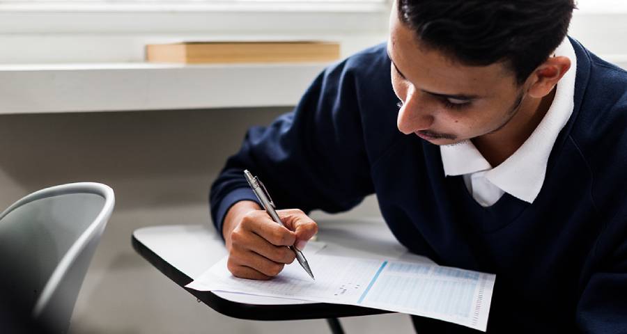 Focused Indian student writing notes in a library preparing for an English proficiency test for Ivy League university application