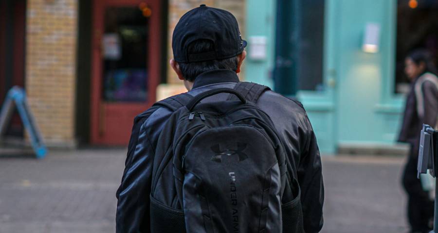 Young person with backpack standing at a crossroads looking forward — representing the thoughtful decision of whether to take a gap year
