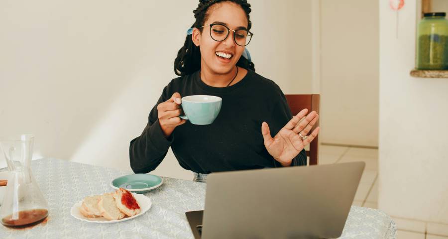 Young woman waving and smiling during a video call on her laptop — staying connected with family in Gujarat while adjusting to life at an Ivy League university