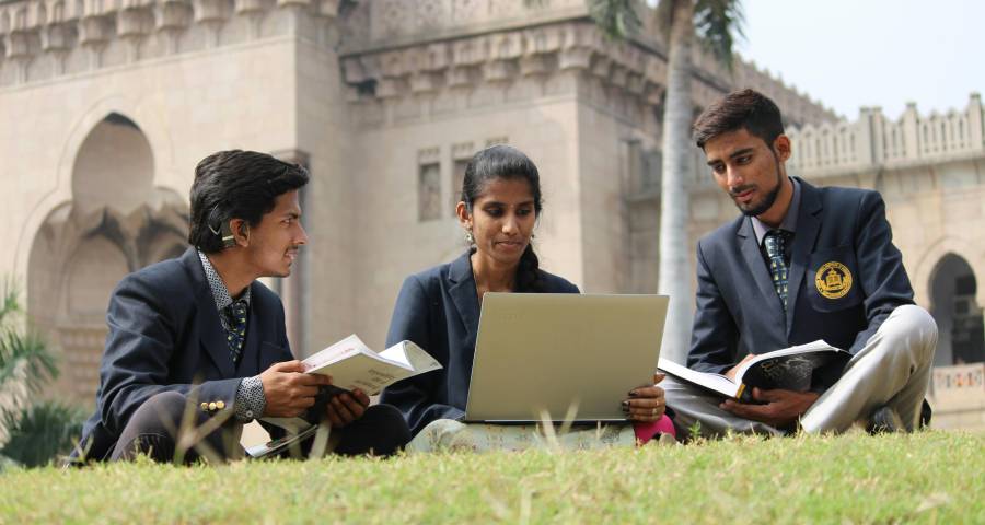 Indian students studying together outside a university building with laptops and books