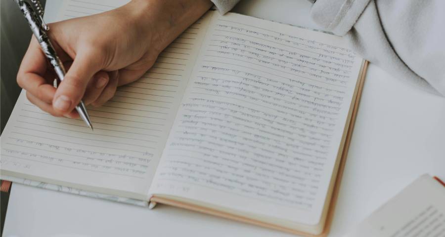 Young woman writing thoughtfully in a notebook — crafting a personal story for her college application 