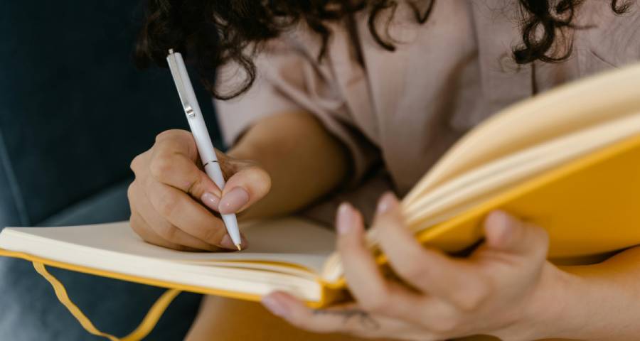 Hands writing in a notebook — practising the show don’t tell technique for a Ivy League personal statement